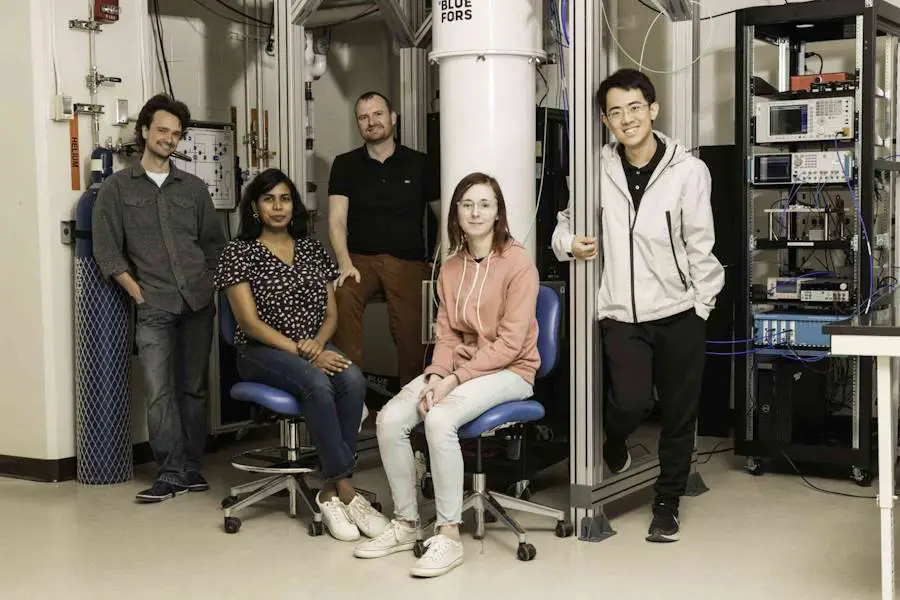 Il professore di fisica e astronomia Machell Block (al centro) e gli studenti di dottorato (da sinistra a destra) Ray Parker, Miherangi Medahin, Liz Champion e Zihou Wang, davanti al frigorifero a diluizione nel laboratorio di Machell Block.  Il team crea circuiti superconduttori che possono essere utilizzati in applicazioni diverse come l'informatica quantistica.  (Foto dell'Università di Rochester/J. Adam Fenster)