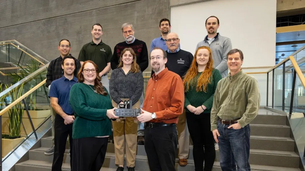 L'équipe du laboratoire de physique appliquée Johns Hopkins se tient ensemble avec son prototype d'antenne. Michael Sherburne, ancien élève, se tient à l'extrême gauche de la dernière rangée.