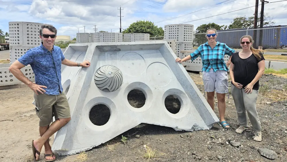 Des chercheurs se tiennent devant un grand brise-lames en béton sur lequel est fixé un module hélicoïdal en creux.