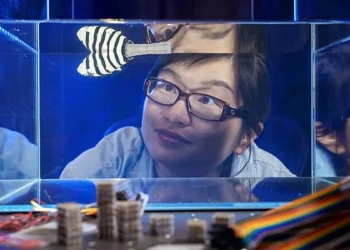 Xiaoyue Ni watches a robotic fish with a reprogrammable tail swim in a fish tank. The proof-of-demonstration could lead