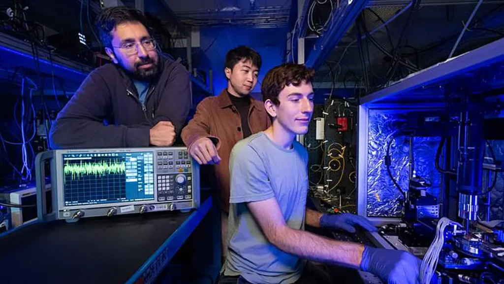 Devin Dean (à droite), doctorant à Stanford, se prépare à mesurer une puce d'amplificateur optique dans le laboratoire d'Amir Safavi-Naeini (à gauche), professeur agrégé de physique appliquée. Dean, Safavi-Naeni et Taewon Park (en haut) sont les coauteurs d'une étude décrivant une nouvelle puce d'amplificateur optique à faible consommation d'énergie qui peut s'intégrer dans des appareils aussi petits qu'un smartphone.