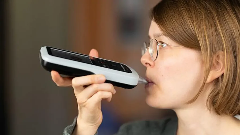 Un utilisateur effectue une mesure de l'acétone dans l'haleine à l'aide d'un analyseur fonctionnant avec un smartphone. (Crédit : Alivion AG)