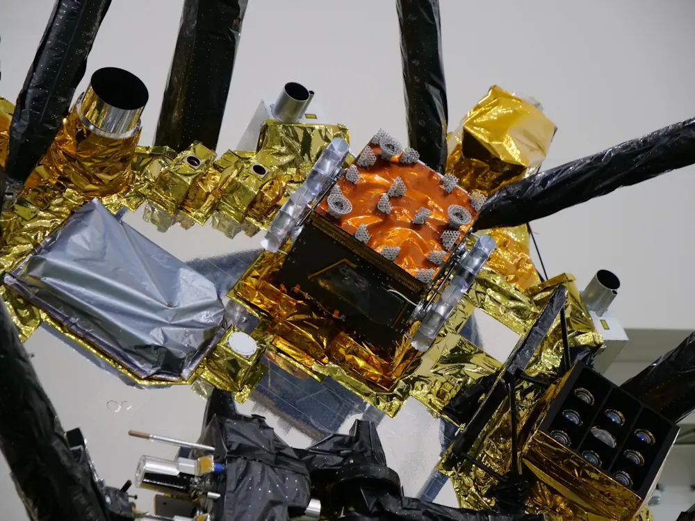 Le rover Idefix® est solidement fixé entre les pieds d'atterrissage de la sonde spatiale MMX. Idefix®, dont la taille correspond à peu près à celle d'une caisse de boissons, est clairement visible dans sa position de déplacement entre les pieds d'atterrissage de la sonde. Malgré sa taille compacte, Idefix® dispose de pratiquement tous les éléments d'un rover scientifique à part entière, bien que sa conception hautement intégrée permette de limiter sa masse à seulement 25 kilogrammes.